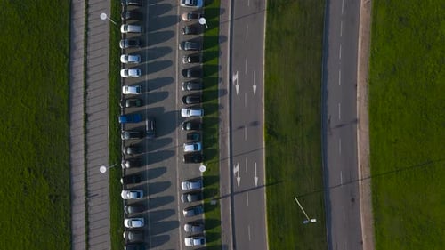 parking lot full of cars with parallel road with lane for cars, free grass separating both, top aeri