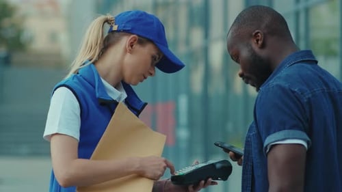 Smiling Young Woman Courier in Blue Hat Hold Package African American Client Paying By Phone for
