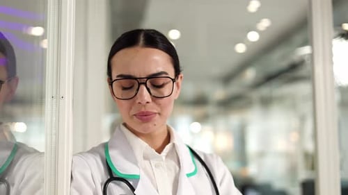 Sad Female Doctor Leaning Against Wall While Feeling Headache in Hospital