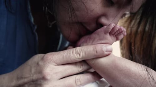 Tender Mother Kisses Newborn Baby Toes with Love