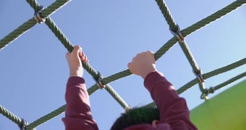 Young boy handing onto rope structure at play park outdoors durining spring - close up on hands