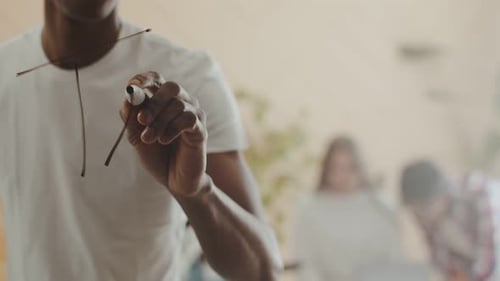 Black Man Writes Word Teamwork on Glass with a Marker Against the Background of Office Workers