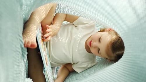 Little Girl Enjoying of Review a Book Under Blue Knitted Plaid in Sunny Morning