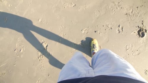 Pov of a young man walking with yellow sport shoes in a beach in summer