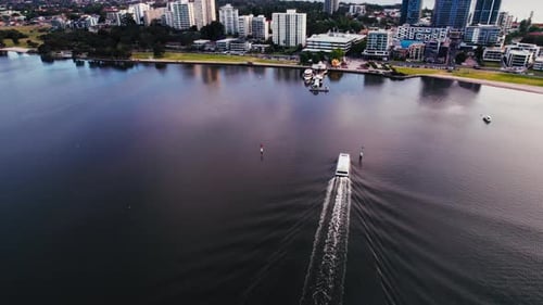 Luftaufnahme eines Schnellboots, das auf einem ruhigen Fluss in der Nähe der städtischen Skyline in der Abenddämmerung fährt
