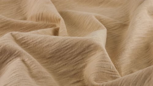 Top view of the soft folds of the thin beige cotton jersey. The textile background rotates