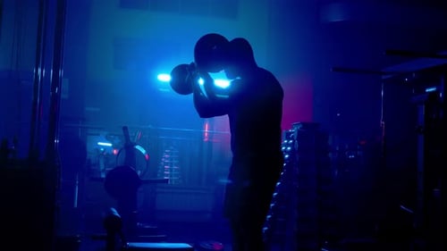 Side View of Dark Silhouette of Bodybuilder Pumping His Arms with Barbell