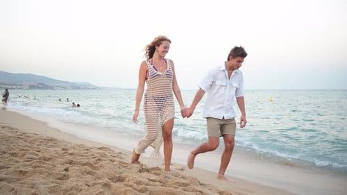 Joyful Couple Walking Hand in Hand Along the Beautiful Sandy Beach During a Warm Summer Evening