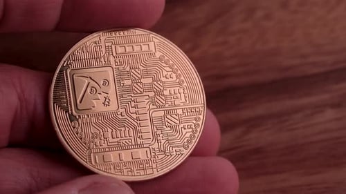 The reverse side of a warm golden bitcoin with light reflections.