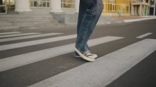 Person Walks Across a Large Crosswalk on a City Street Wearing Casual Clothes and Sneakers on a