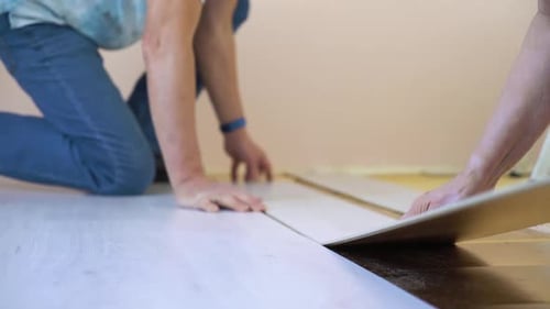 Adults Installing Laminate Wood Flooring Indoors