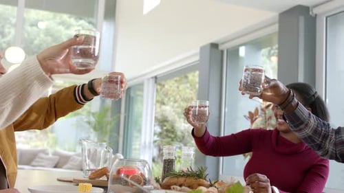 Amigos diversos estendendo os braços, tostando copos na mesa, bebendo água, servindo salada, espaço para cópias