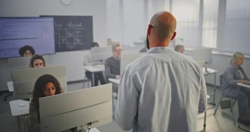Professional Male Instructor Stands in Front of Adult Students in Computer Lab Explaining Coding