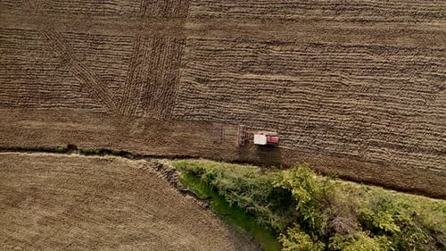Farmer plowing field with tractor and harrow, aerial view of soil preparation in agriculture.