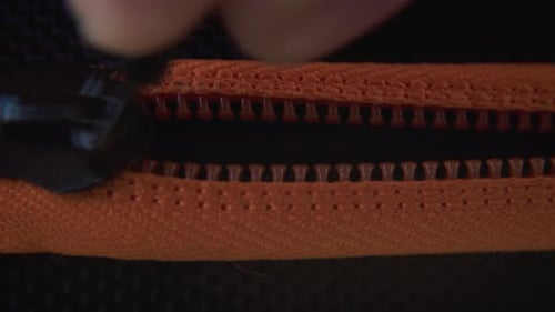 A cinematic close-up shot of a hard case zipper being closed, orange rexture, metal zip, black box,
