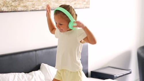 Happy Young Girl Dancing with Headphones on Bed