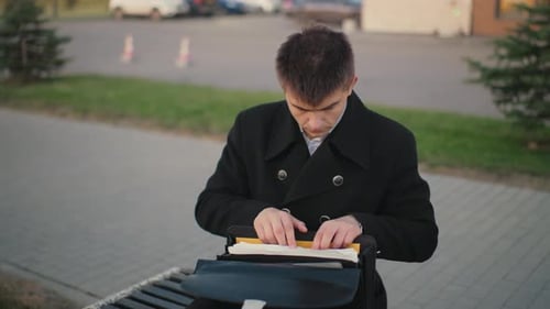 Young Man Searches Through Briefcase on Bench