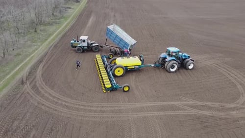 Blue tractor with yellow seeder working on the field in Ukraine OA