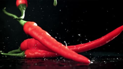 Chili Peppers fallen auf einen nassen schwarzen Tisch, gefilmt mit einer Hochgeschwindigkeitskamera mit 1000 Bildern pro Sekunde