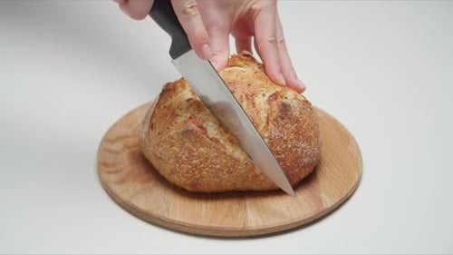 Closeup of Female Hands Cutting Fresh Baked Bread with a Sharp Knife