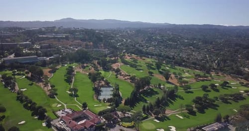 Aerial drone footage of golf grounds and tennis court mountains in background flying forward