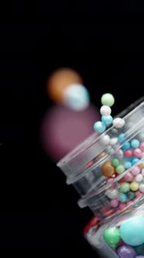 Vertical video. Sugar Balls of Different Colors and Sizes Fall onto the Table, Slow-Motion.