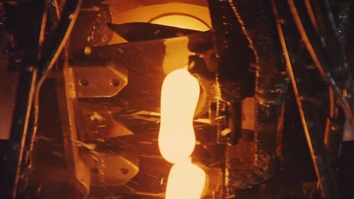 Slow motion of Molten glass pouring out of a Glass melting furnace in a bottle production facility.