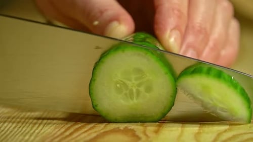 Close-up of female hands cutting cucumber in the kitchen