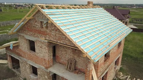 Aerial View of a Brick House with Wooden Roof Frame Under Construction