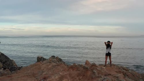 Flyover of a woman on the beach and then towards the endless ocean horizon at sunset