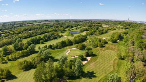 Aerial drone view of a green golf course set within a wooded countryside. Trees dot the manicured