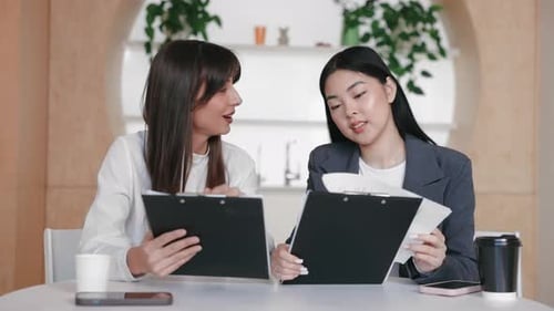 Engaged Teammates Reviewing Notes on Clipboards While Chatting Across Table in Casual Tone
