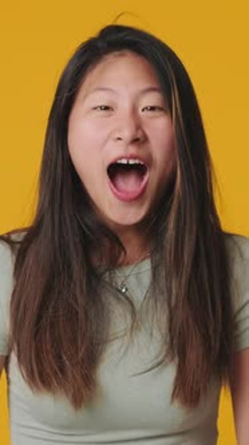 Young woman clapping in hand looking at camera, isolated over yellow background in studio