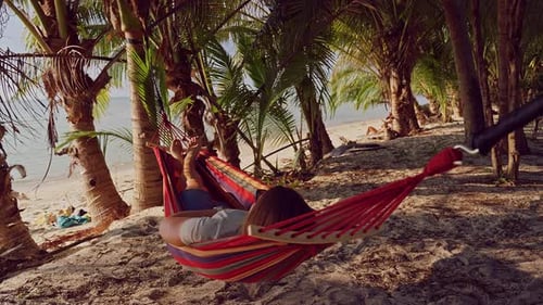 First person view from hammock with legs extended under palm trees near tropical beach creating pers