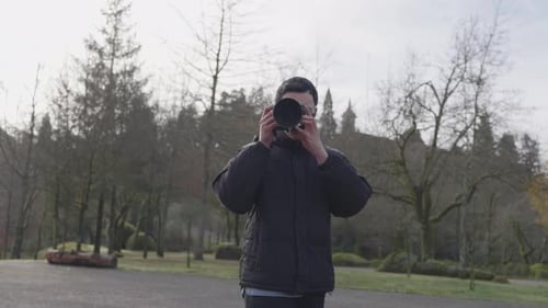 Man raising camera to eye in park walkway