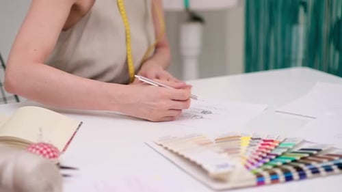 Lady Dressmaker with Tattoo Draws Clothes Model on Paper at Desk in Fashion Atelier Tailor at Work