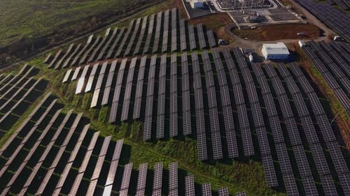 Solar panels cover a large field during daylight hours near energy facility