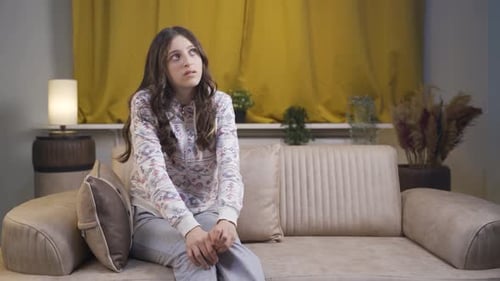 Anxious Young Woman Sits on a Couch Looking Around