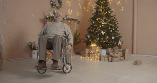 Senior Man Sits in Wheelchair Near Christmas Tree