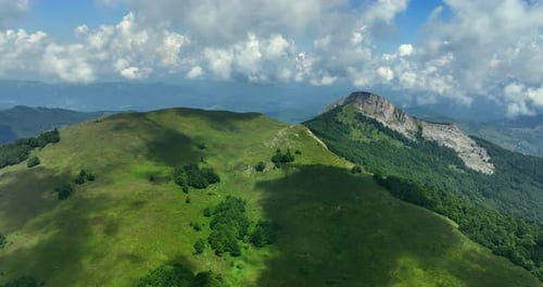 Flight over green mountain peaks. A beautiful sunny summer day at high altitude with thick clouds an