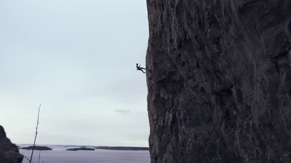 Man rappelling down a vertical mountain, ocean view in background ...