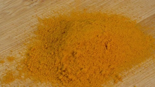 Turmeric powder spice fall down and rotate on wooden background. Dry seasoning turmeric. Spices
