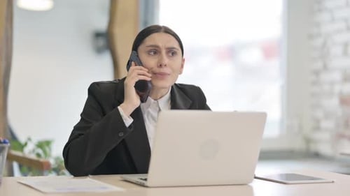 Frustrated Woman Talking on Mobile Phone in Office