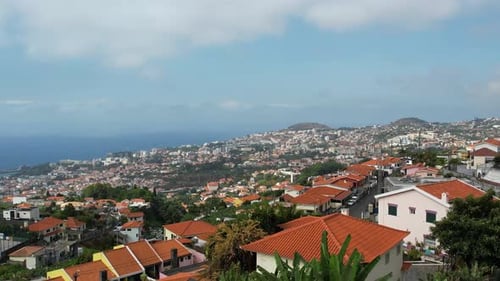 Aerial ascending view over hillside city with Atlantic Ocean in distance, island capital panorama