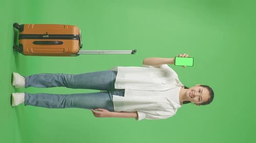 Asian Female Traveler With Luggage Smiling And Showing Green Screen Smartphone In The Green Screen