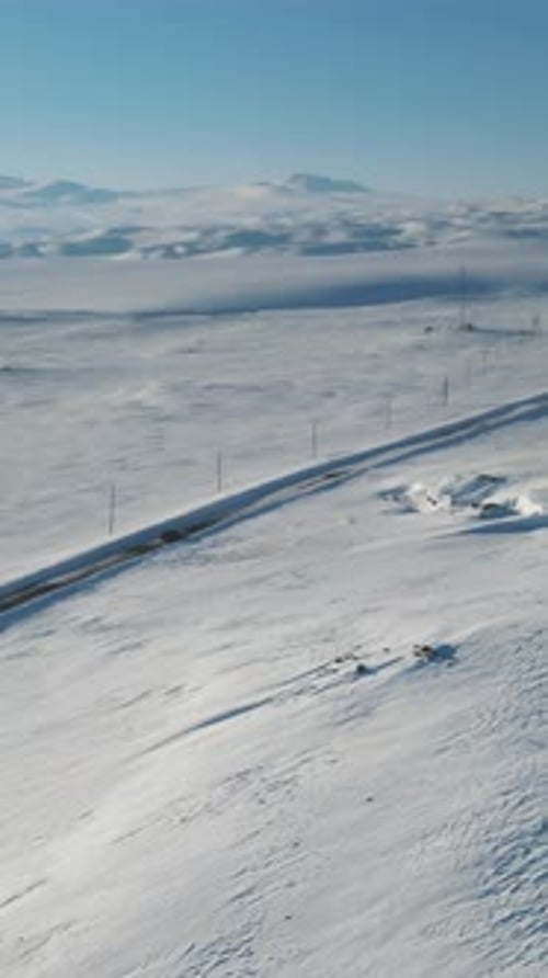 Gefrorene Autobahn unter strahlend azurblauem Himmel mit Strommasten, darunter erstreckt sich eine ruhige, schneebedeckte Straße