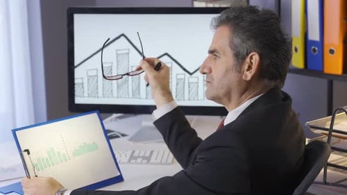 Mature businessman analyzing graphs in his office. Period profit or loss graphs, statistics.