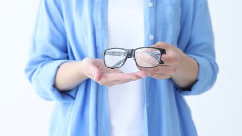 Woman showing pair of glasses on white background, closeup