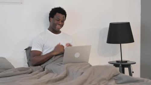 Young Adult Using Laptop in Bed for Video Call