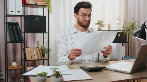 Focused Indian Office Worker Working with Schedules and Financial Graphics While Using Calculator